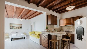 A modern kitchen with wooden beams, a dining area with a yellow sofa, and a bed with white linens. - One-Bedroom Apartment with Private Terrace and Air Conditioning (Marinella di Selinunte)