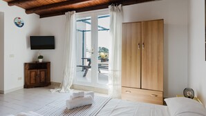 A bedroom with a wooden ceiling, a TV on the wall, a wardrobe, and a window with curtains. - One-Bedroom Apartment with Private Terrace and Air Conditioning (Marinella di Selinunte)