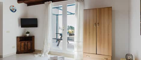 A bedroom with a wooden ceiling, a TV on the wall, a wardrobe, and a window with curtains.