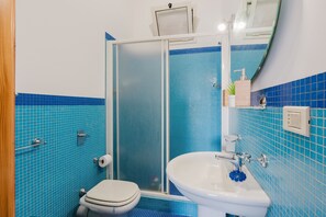 Une salle de bain avec douche, toilettes et lavabo, le tout agrémenté de murs recouverts de carreaux bleus.