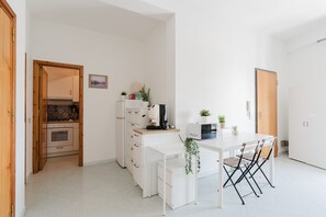 Une cuisine compacte avec des meubles blancs, un four à micro-ondes, une machine à café et une petite table à manger avec des chaises.