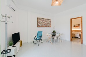 Une chambre moderne équipée d’un téléviseur à écran plat, d’un fauteuil bleu, d’une petite table à manger avec des chaises, d’un élément décoratif mural et d’une porte en bois donnant sur une autre pièce.
