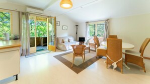 En rummelig stue med sofa, spisebord, stole og et stort vindue med udsigt til grønne omgivelser.