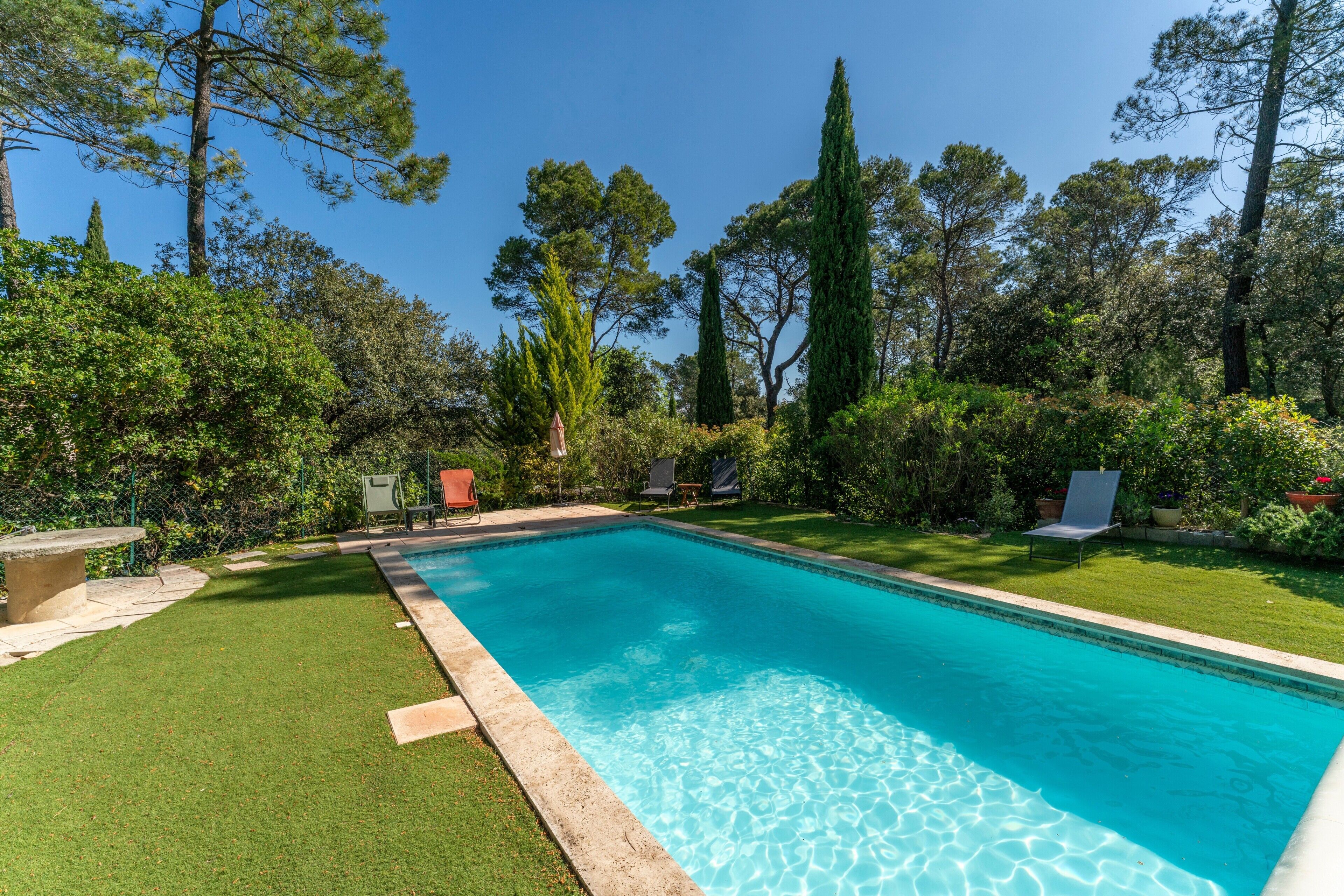 Una piscina rectangular con agua cristalina azul, rodeada por un césped cuidado y árboles.