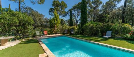 Una piscina rectangular con agua cristalina azul, rodeada por un césped cuidado y árboles.