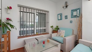 A room with a glass coffee table, wicker furniture, a window with bars, and decorative items on the walls.
