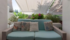 A light blue sofa with floral cushions, a white wall, and a view of greenery.