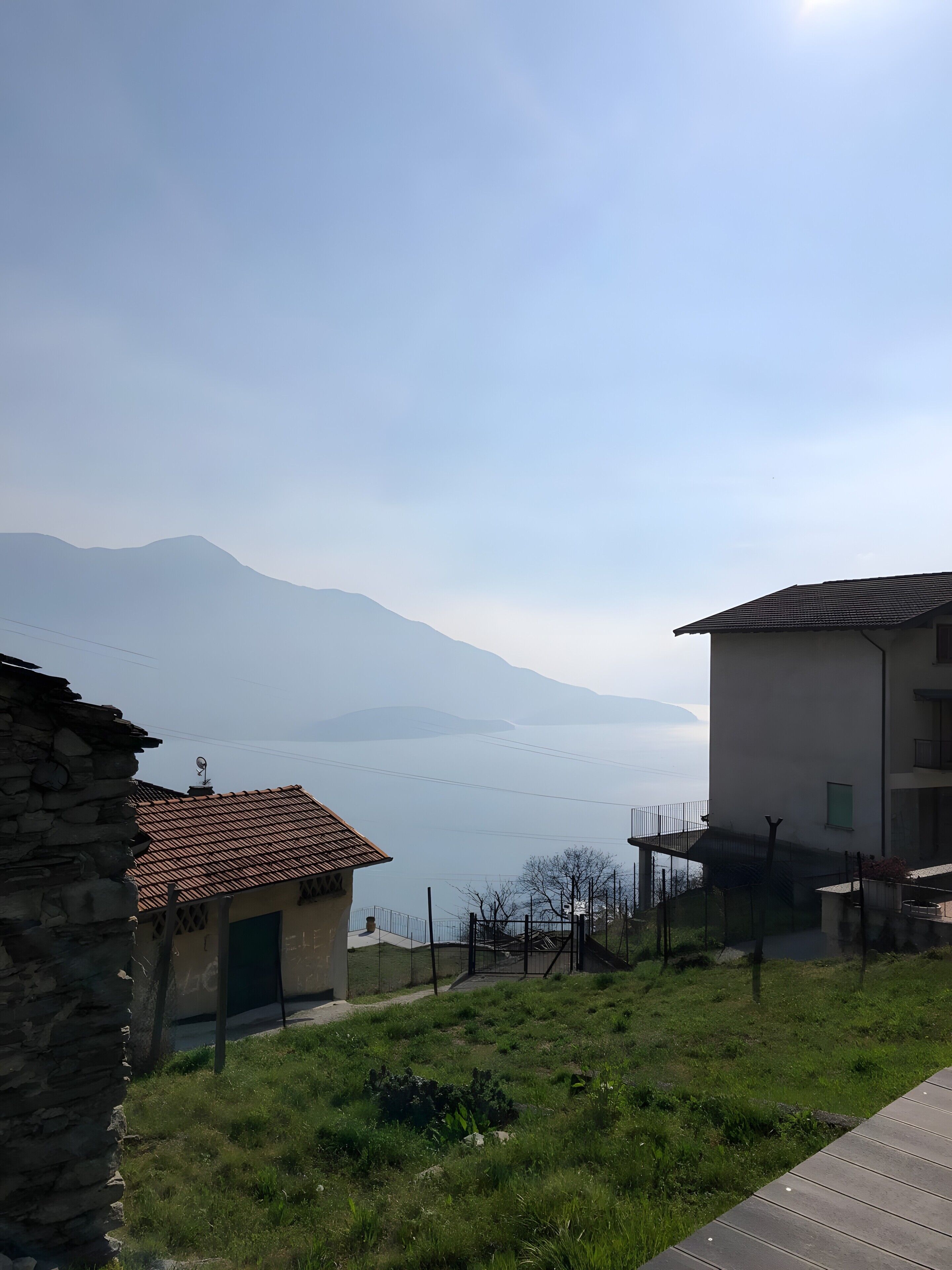 A view of a mountainous landscape with a body of water in the distance, a stone building, and a modern building with a balcony.