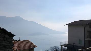 A view of a mountainous landscape with a body of water in the distance, a stone building, and a modern building with a balcony.