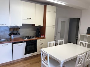 A compact kitchen with white cabinets, a gas stove, a coffee maker, and a dining table with chairs. - Holiday Apartment '4' with Lake View, Shared Pool and Wi-Fi (Montemezzo)
