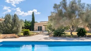 A swimming pool with a stone wall, a building with a tiled roof, and surrounding trees.