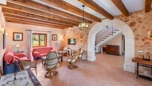 A spacious living area with a stone wall, wooden beams, a staircase, and a sofa.
