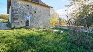 A stone house with a sloped roof, a small porch, and a grassy yard. - Traditional and Organic Gîte in the Tude Valley – Nature, Comfort, and Relaxation (Montboyer)