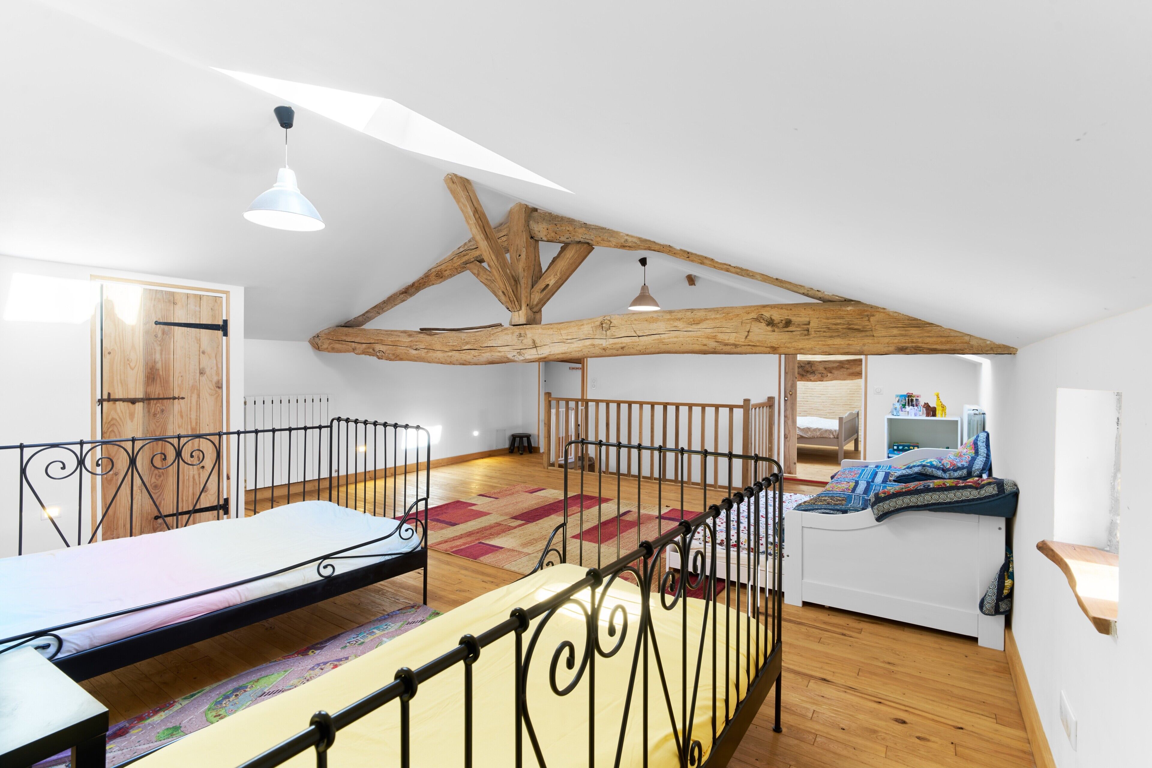 Camera mansardata con soffitto alto, travi a vista in legno, un letto a castello, una scrivania e un piccolo angolo salotto.