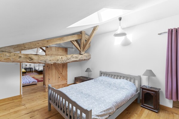 Una camera da letto con soffitto spiovente, travi in legno, un letto, comodini e un lucernario.