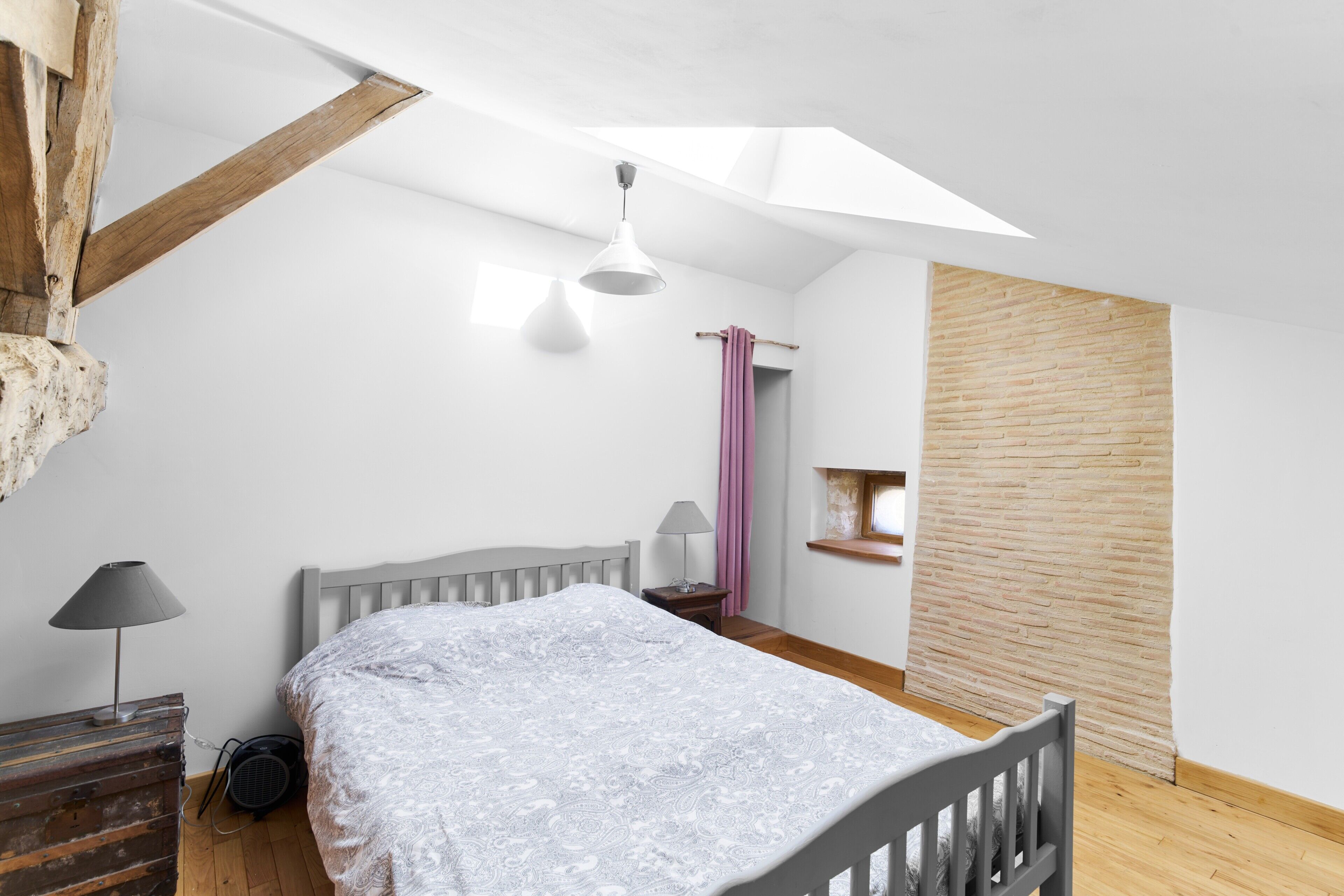 Un dormitorio con techo inclinado, una cama, una mesita de noche con lámpara, una ventana con vistas y una pared de madera decorativa.