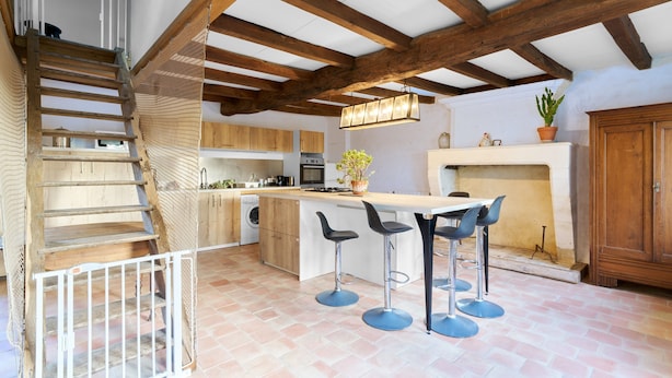 A kitchen with wooden beams, a staircase, and a bar area with stools. - Traditional and Organic Gîte in the Tude Valley – Nature, Comfort, and Relaxation (Montboyer)
