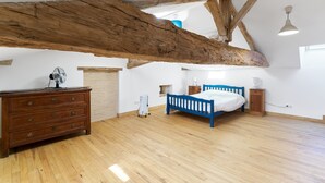 A spacious room with a wooden ceiling beam, a bed, a dresser, and a fan. - Traditional and Organic Gîte in the Tude Valley – Nature, Comfort, and Relaxation (Montboyer)