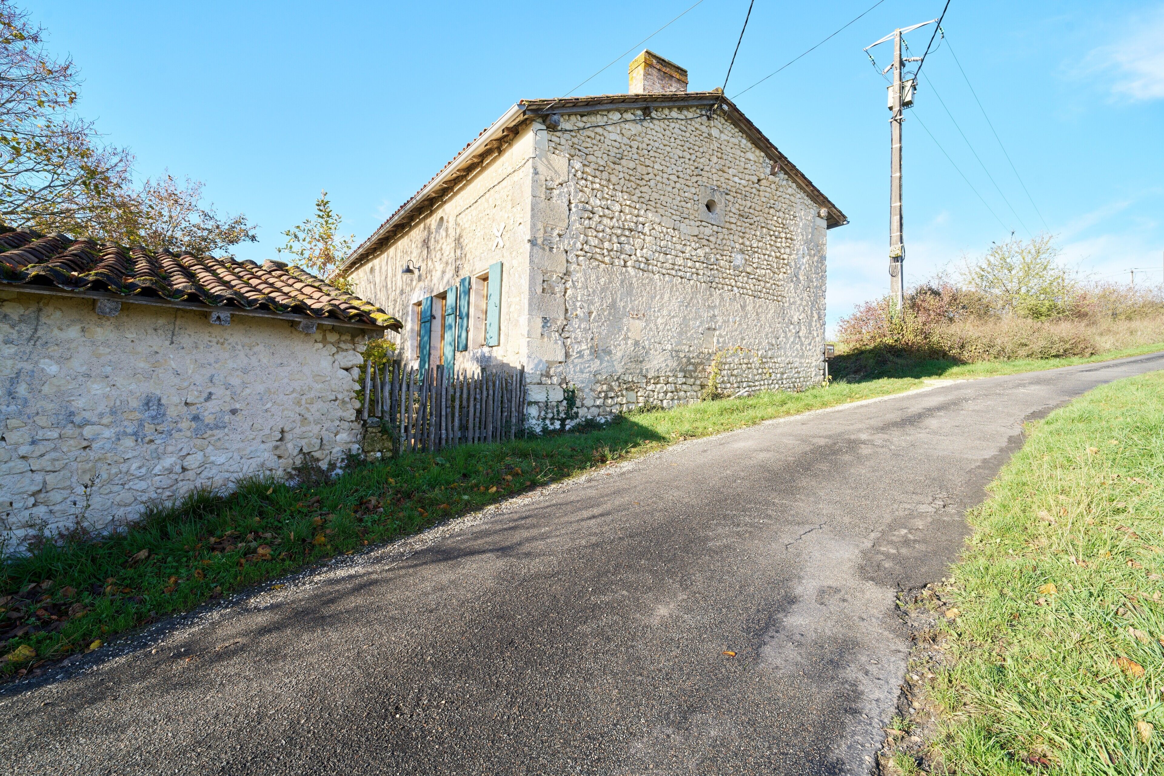 A stone building with a tiled roof, a narrow road, and a utility pole.