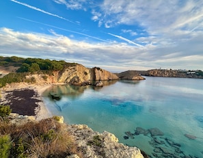 A coastal landscape with clear waters, rocky cliffs, and a distant shoreline with buildings. - Holiday Home 'Tres' with Private Pool, Private Terrace and Wi-Fi (Es mercadal)