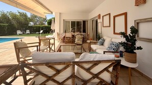 A sunlit patio with outdoor furniture, a pool, and a view of the greenery.