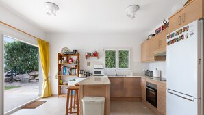 A modern kitchen with a central island, wooden cabinets, a refrigerator, and a view of greenery outside.