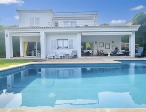 Ein zweistöckiges Haus mit Swimmingpool, Außenmöbeln und einer überdachten Terrasse.