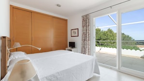 A bedroom with a bed, a TV, a wardrobe, and a balcony with a view.
