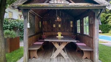 Un pavillon rustique en bois, doté d’une table et de bancs, entouré d’un jardin et d’une piscine.