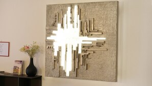 Una obra de arte abstracto en la pared con formas geométricas y un florero con flores sobre un escritorio.