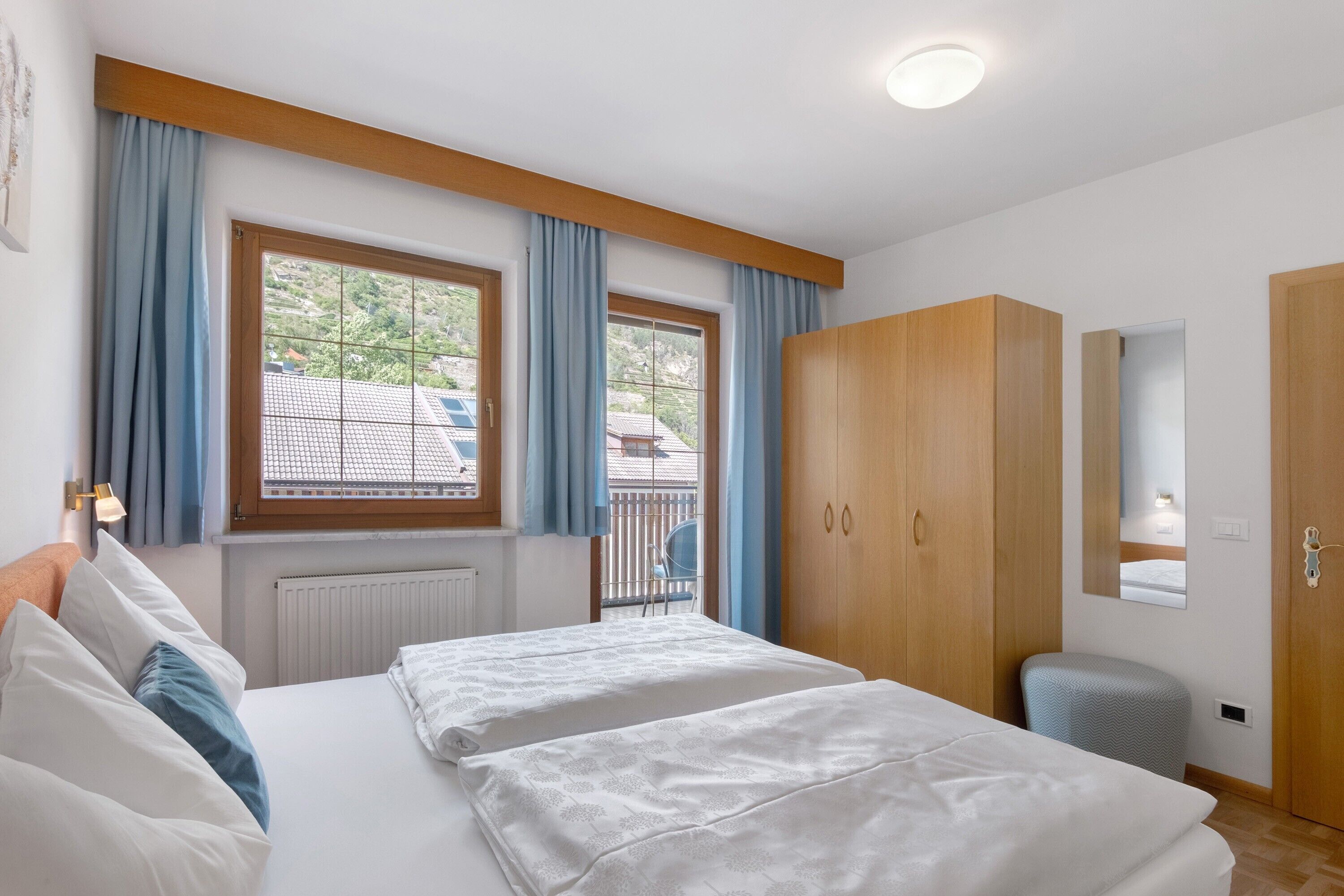A bedroom with two beds, a wardrobe, a radiator, and a window with curtains.