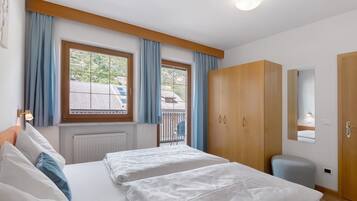 A bedroom with two beds, a wardrobe, a radiator, and a window with curtains.