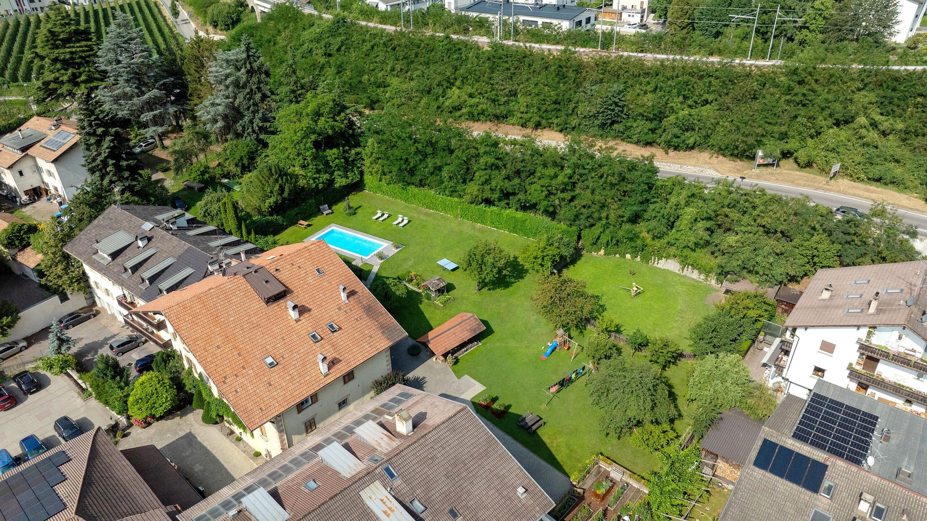A residential area with a swimming pool, green lawns, and solar panels on rooftops.