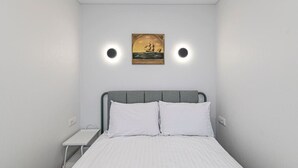 Un dormitorio con una cama, dos mesitas de noche, un buró, un cuadro colgado en la pared y dos lámparas de pared.