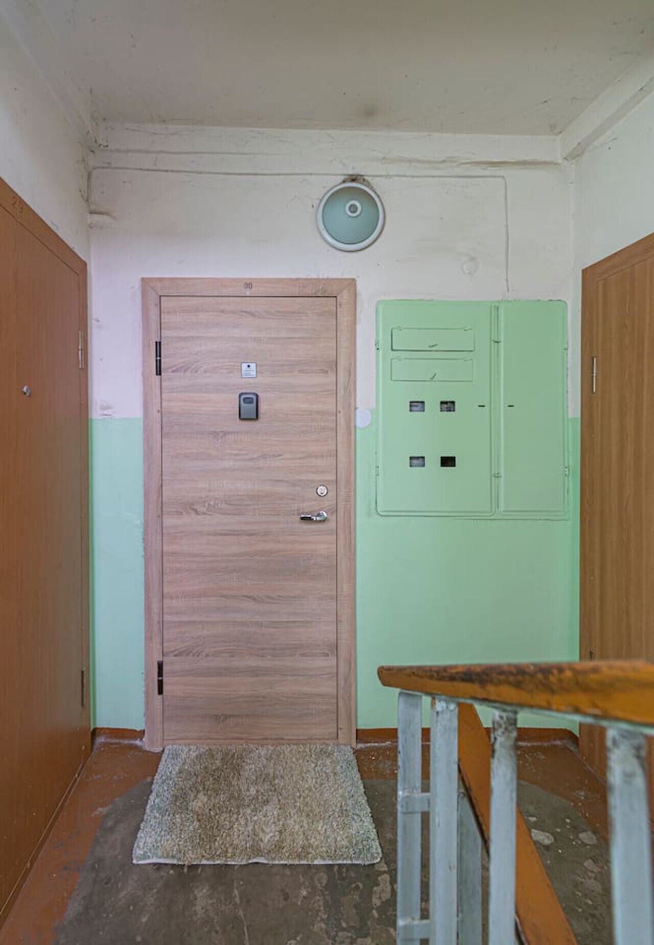 Una habitación con una puerta de madera, un cuadro de distribución verde y una pequeña mesa con una silla.
