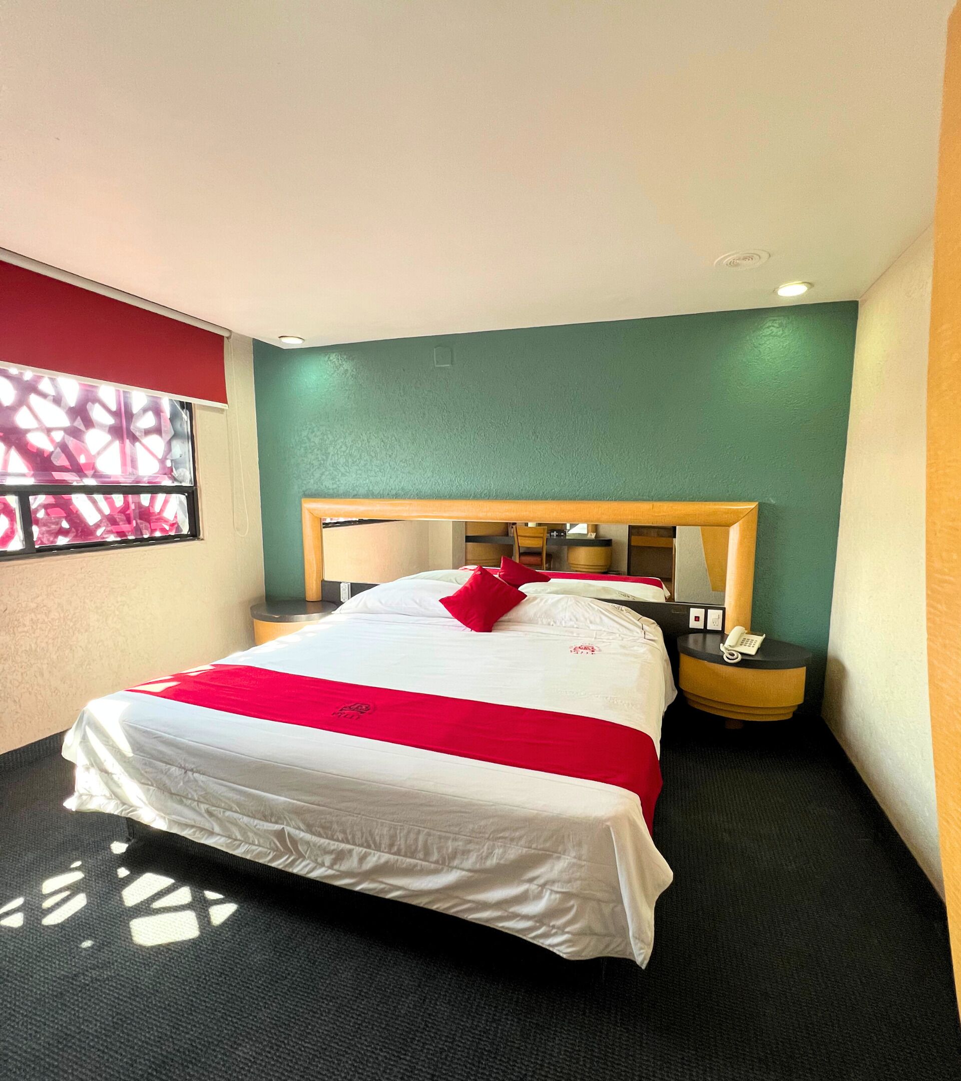 A hotel room with a large bed, a bedside table with a phone, and a window with a view of the outside.