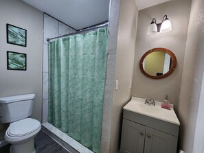 A bathroom with a toilet, a shower with a green patterned curtain, a sink with a mirror above it, and two wall-mounted lights.
