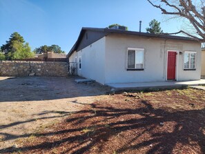 A small, single-story house with a red door, a stone wall, and a clear sky.