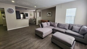 En rummelig opholdsstue med en hjørnesofa, et spisebord og et køkkenområde.
