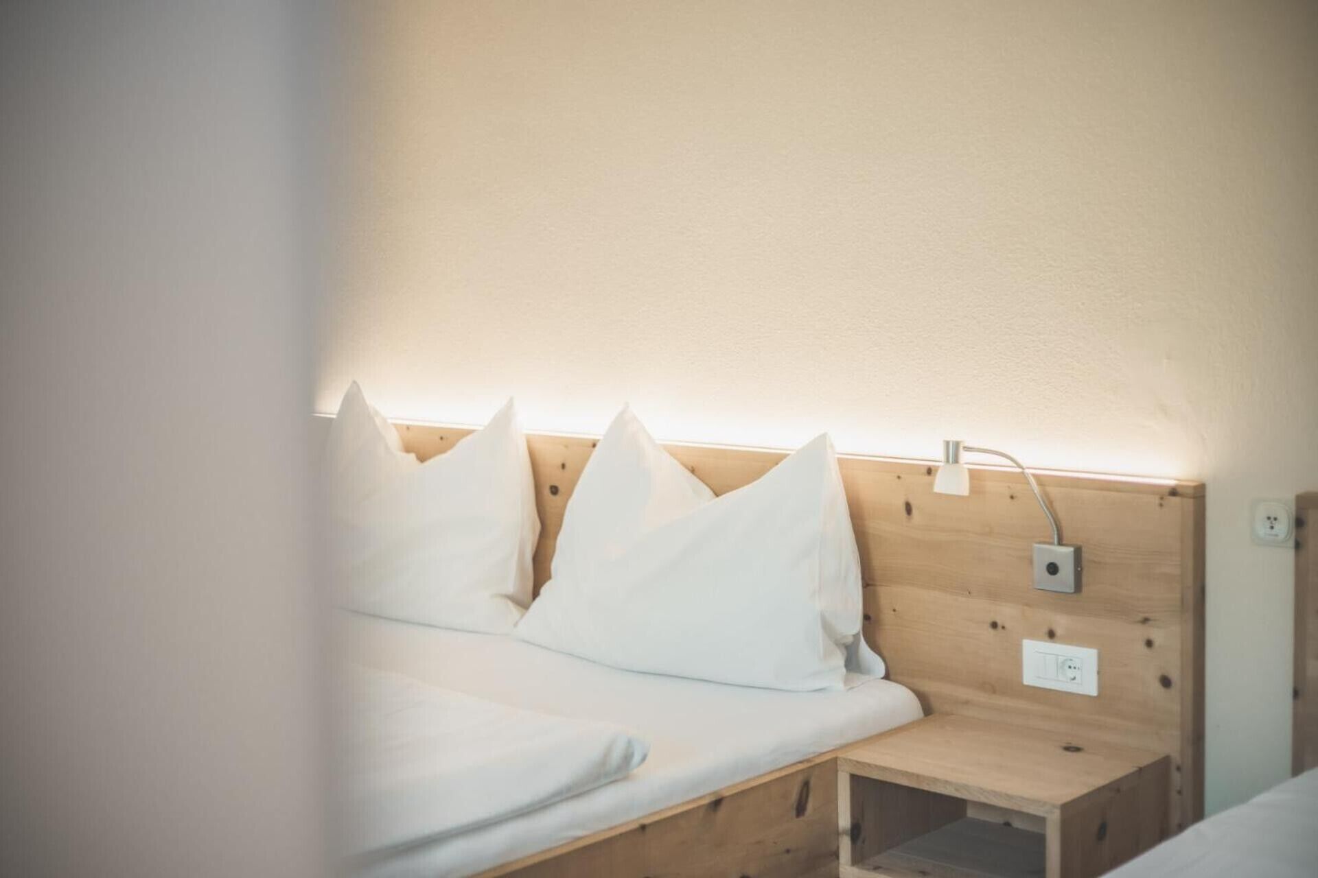 A bed with white bedding, a wooden headboard, and a bedside table with a lamp.