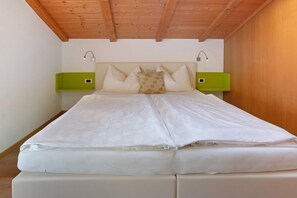 A bed with white bedding, two nightstands with green side tables, and a wooden ceiling.
