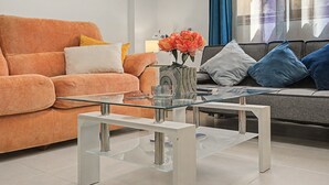 Uma sala de estar moderna com uma mesa de centro de vidro, sofá laranja e sofá cinza com almofadas azuis.