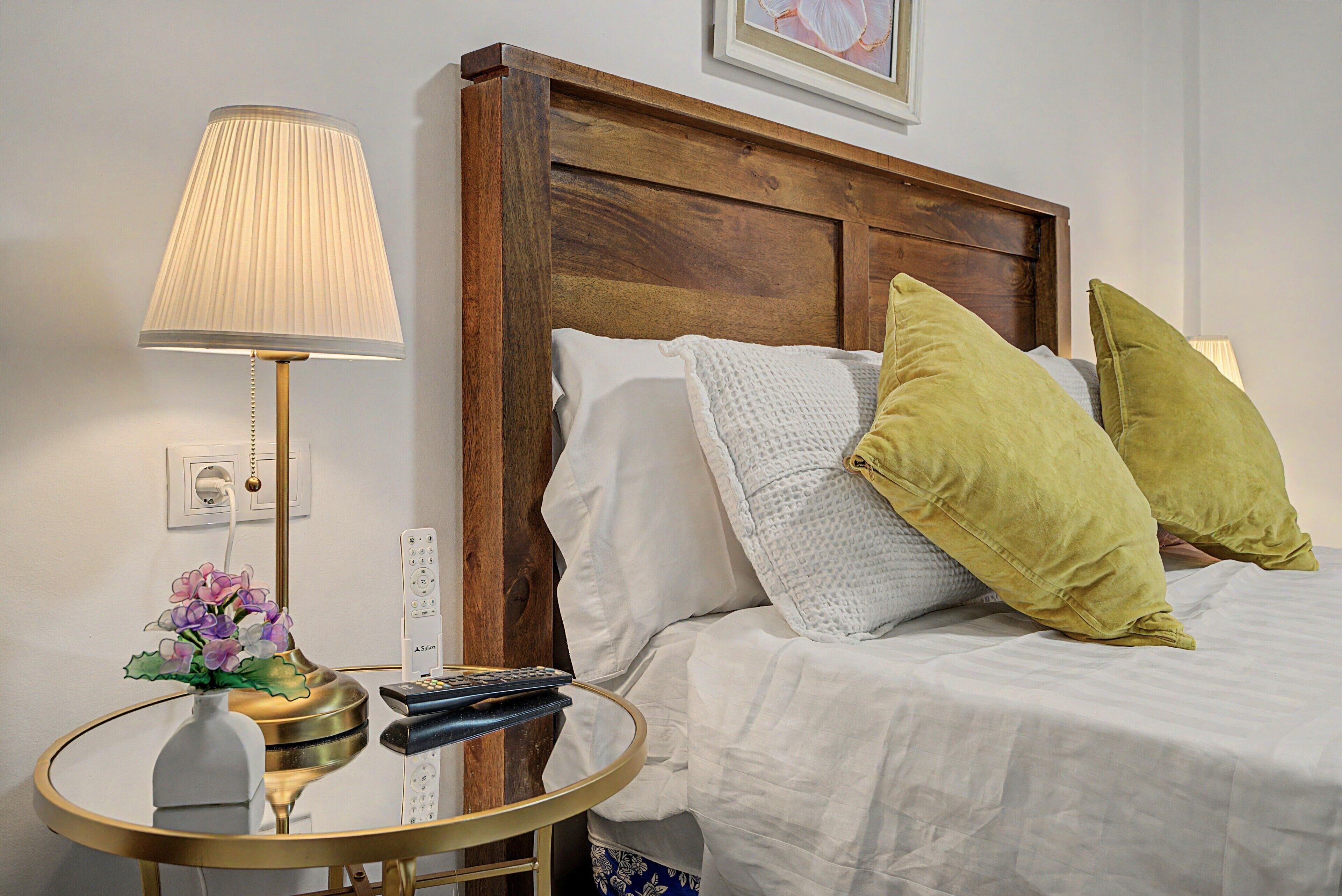 Une chambre d’hôtel avec une tête de lit en bois, une table de chevet avec une lampe, une télécommande et des coussins décoratifs.
