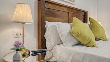 Une chambre d’hôtel avec une tête de lit en bois, une table de chevet avec une lampe, une télécommande et des coussins décoratifs.