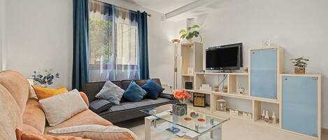 A modern living room with a sofa, coffee table, TV, and shelving unit.