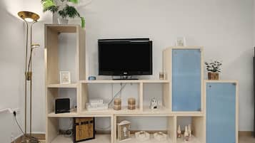 Una habitación con una televisión sobre un mueble bajo, una planta y un armario con diversos objetos.