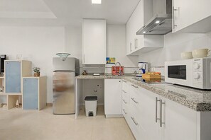 A kitchen with white cabinets, a stainless steel refrigerator, a microwave, and a sink.