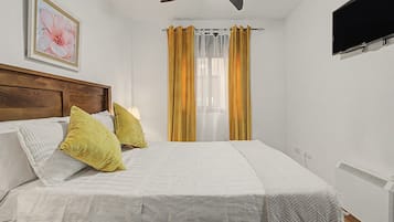 Una habitación de hotel con una cama, cabecera, televisor montado y un cuadro en la pared.