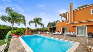 Ein Schwimmbecken mit Rutsche, Liegestühlen und einer umzäunten Terrassenanlage.