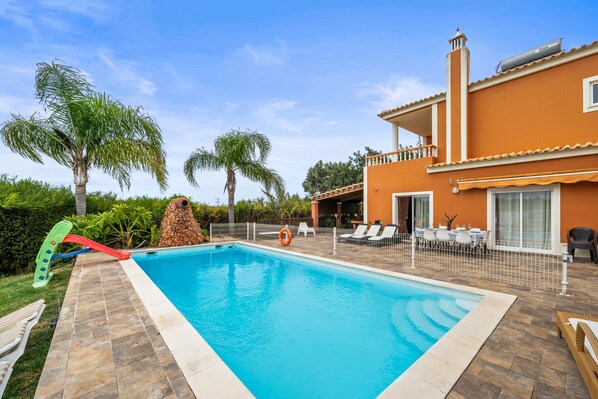 Une piscine avec un toboggan, des chaises longues et un patio clos.